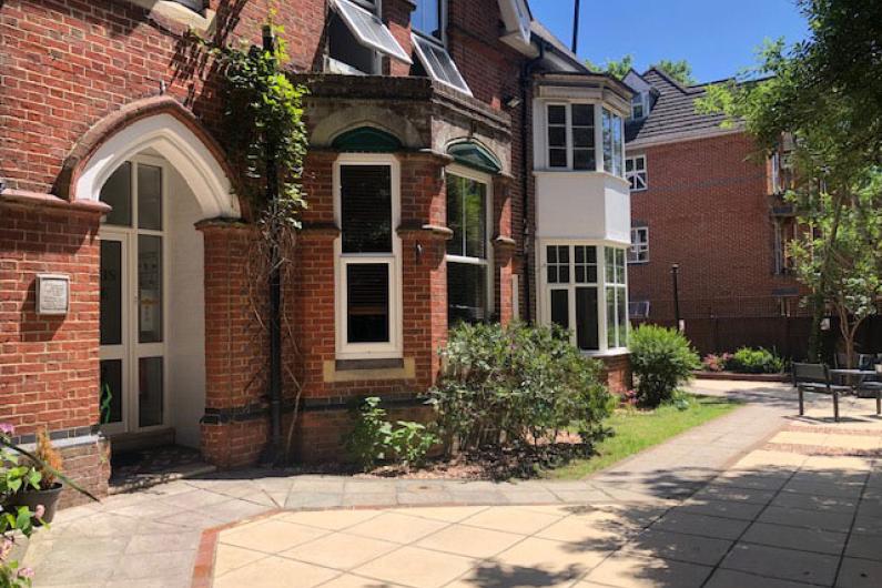 A photo of the outside of a building. It is red brick with multiple bay windows and a patio out the front.