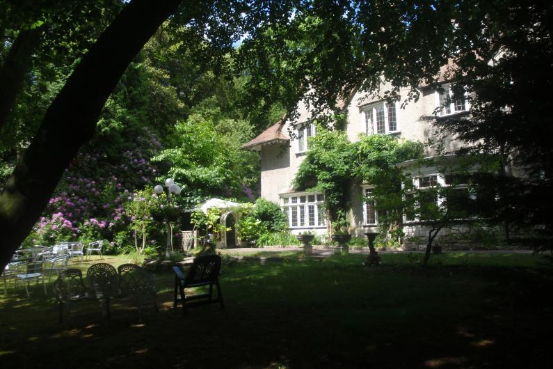 A shady view from the garden, including the main building in the background, which has plants growing up it