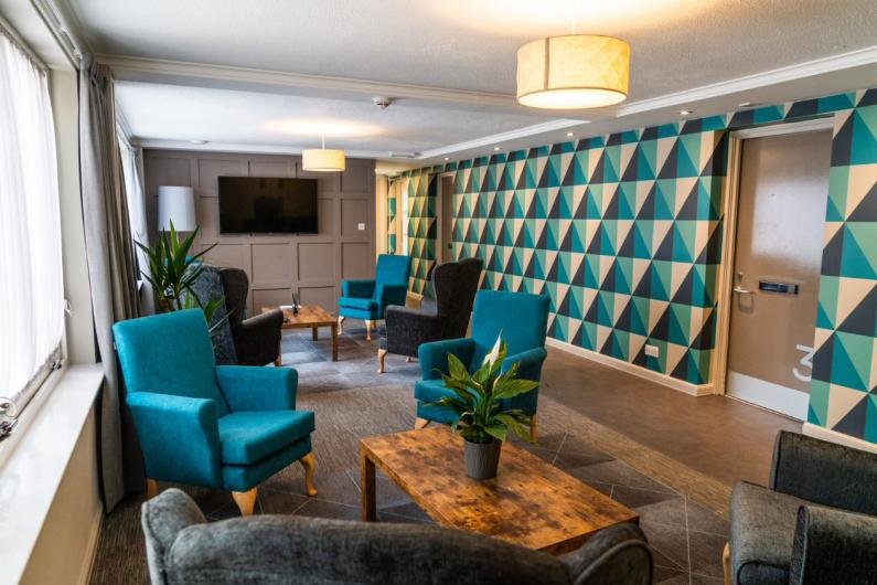Group space - a room with teal wingback chairs, a TV and teal and green wallpaper