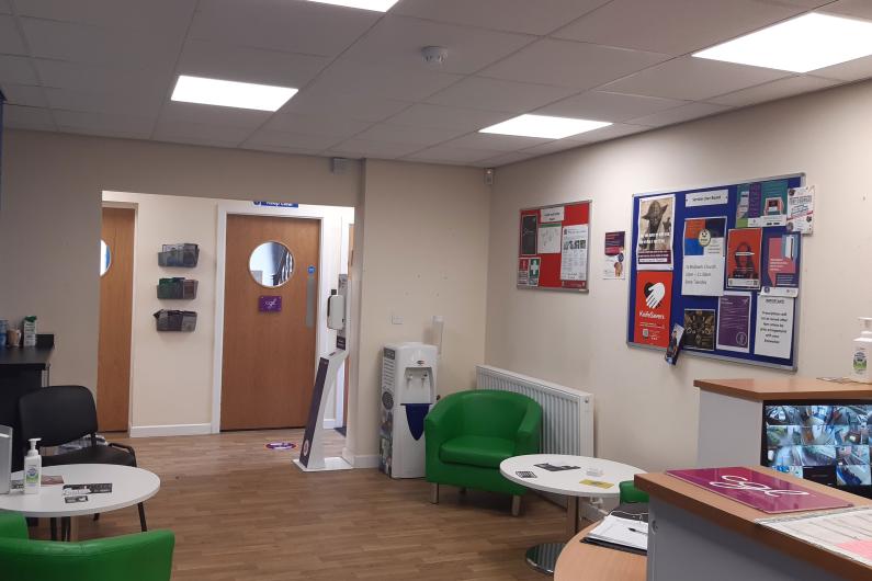 The Macclesfield Reception Area - a room with white walls, green seating and a display board