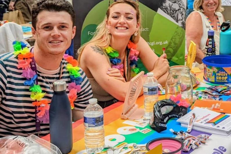 A man and two women smiling at the camera sat behind a table with leaflets on it.