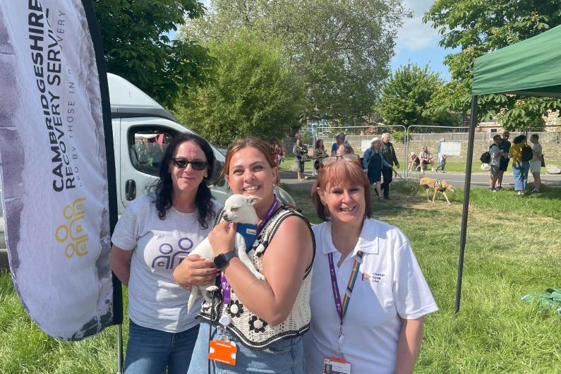 three women smiling at the camera, the middle woman is holding a small dog.