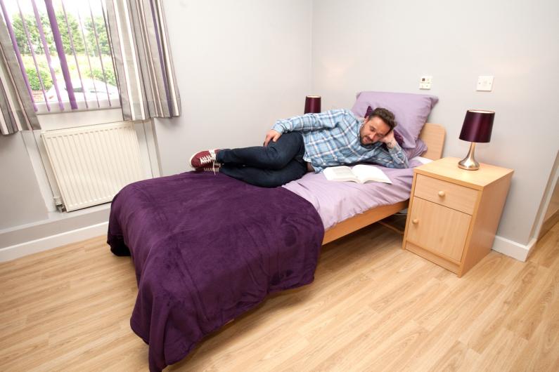 New beginnings - national detox framework - bedroom. A person lying on a single bed with purple sheets. The room is bright with light wooden floors