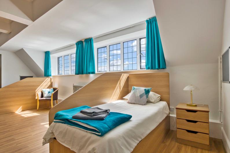 Clouds House - national detox and rehab framework. A bedroom with cyan curtains and sheets, two single beds and privacy screens, it is bright and airy with light wood