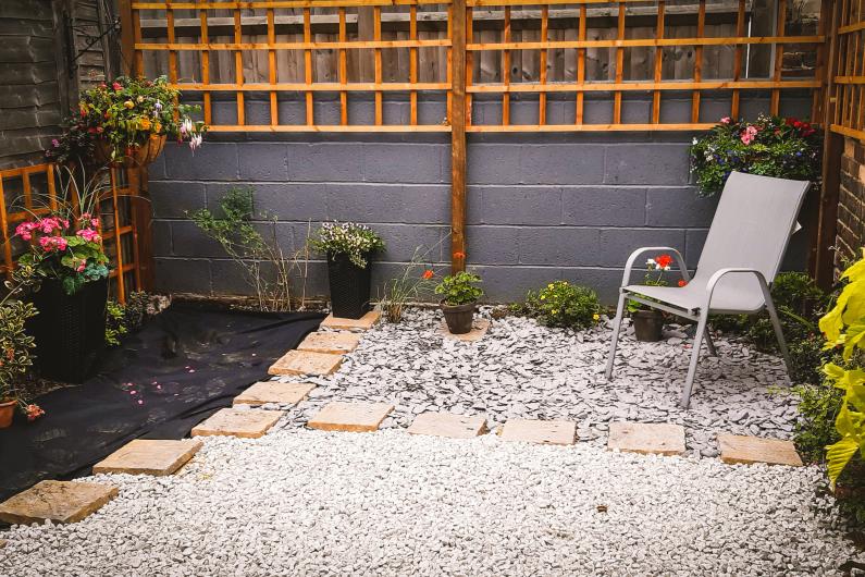 A garden with plants around the edge, a garden chair in the corner and gravel spread across the floor. 