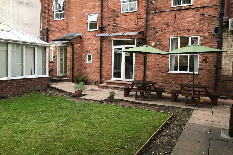 A garden with a conservatory and two wooden picnic benches.