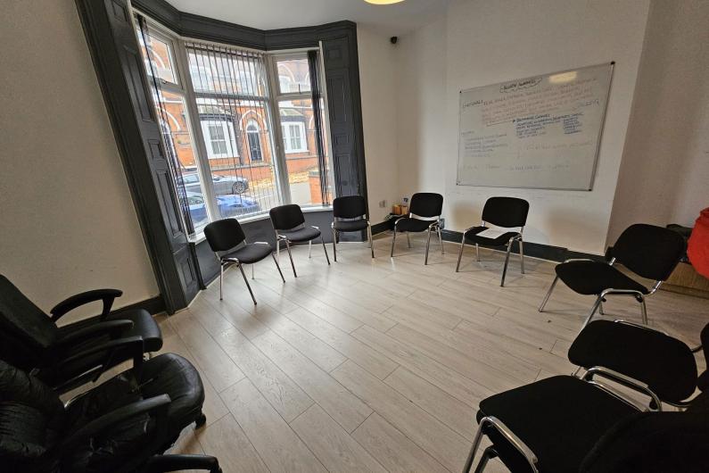 A room with big bay windows on one wall. There are chairs lining the edge of the room.