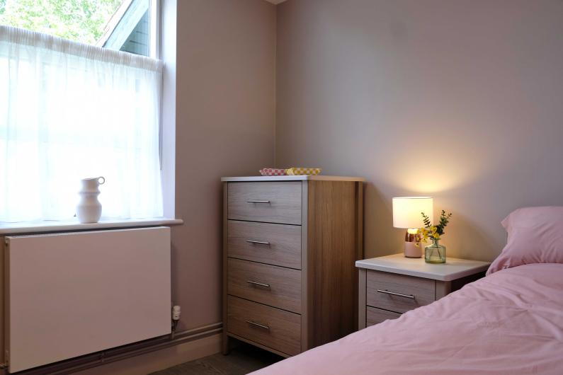 A bedroom with a bed, chest of drawers and bedside table next to a window