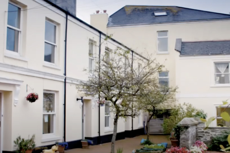 The outside of a white painted building. It has a courtyard with a few trees around it