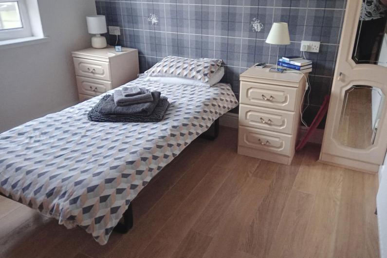 A single bed in a room with a bedside table either side and a wardrobe.