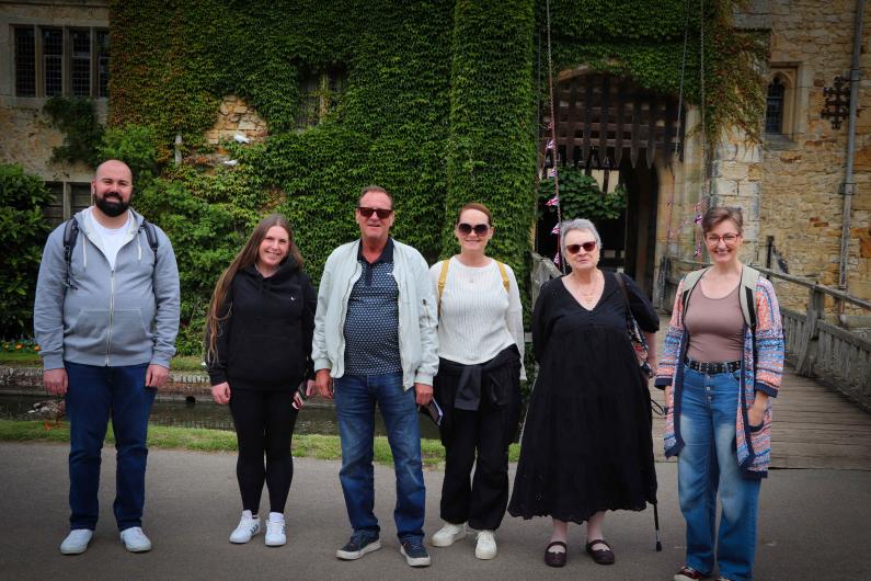 six people stood posing for a photo. Behind them is an old wall with plants trailing up it