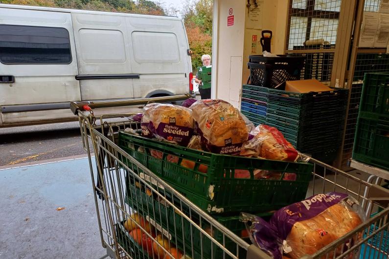 A shopping trolley full of food in the entrance of a warehouse with a white van parked outside