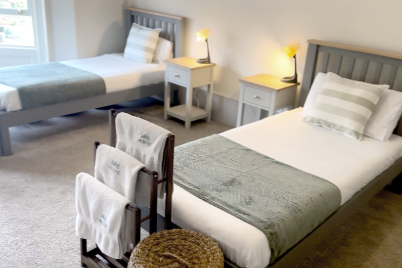 Two single beds, each with a basket and towels at the foot of the bed and a bedside table with a lamp