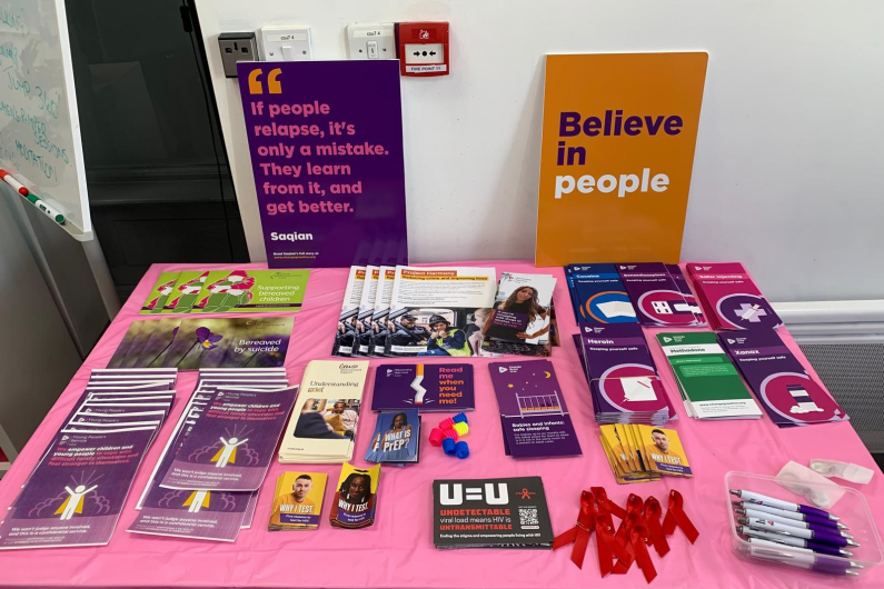 A table with a pink table cloth holding leaflets and merchandise on it