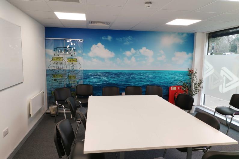 A room with a mural of the sea on the back wall, and a table in the centre with chairs around it.