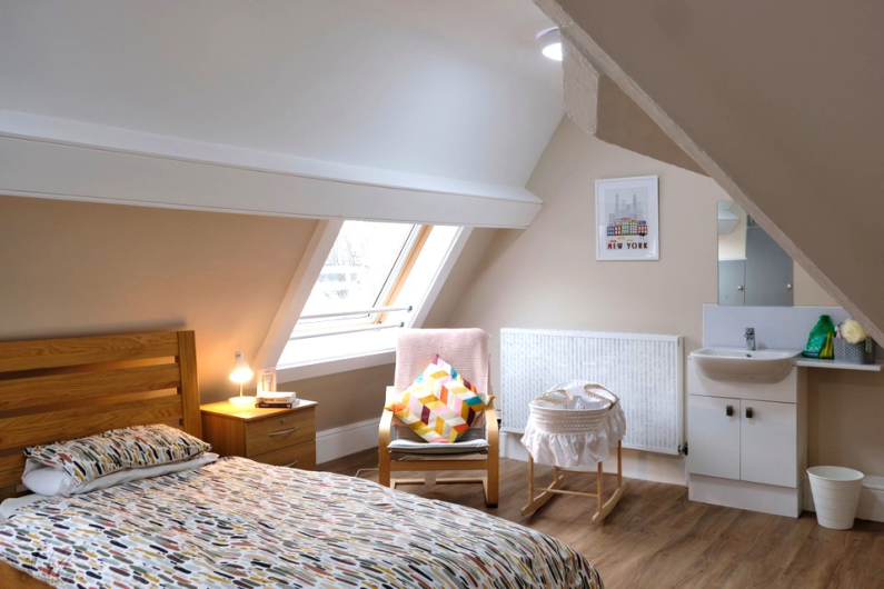 A bedroom with slanted ceilings. There is a single bed with a sink and a Moses basket