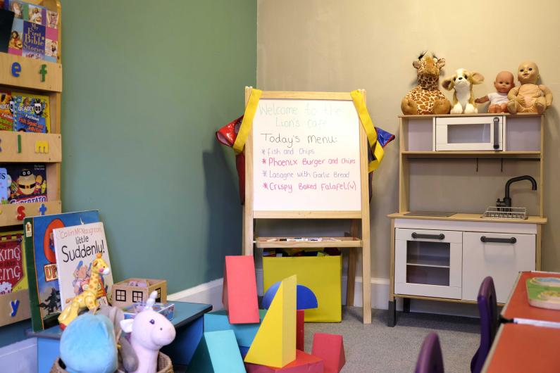 A play area with a whiteboard with a menu written on it. Kids toys are scattered around the room.